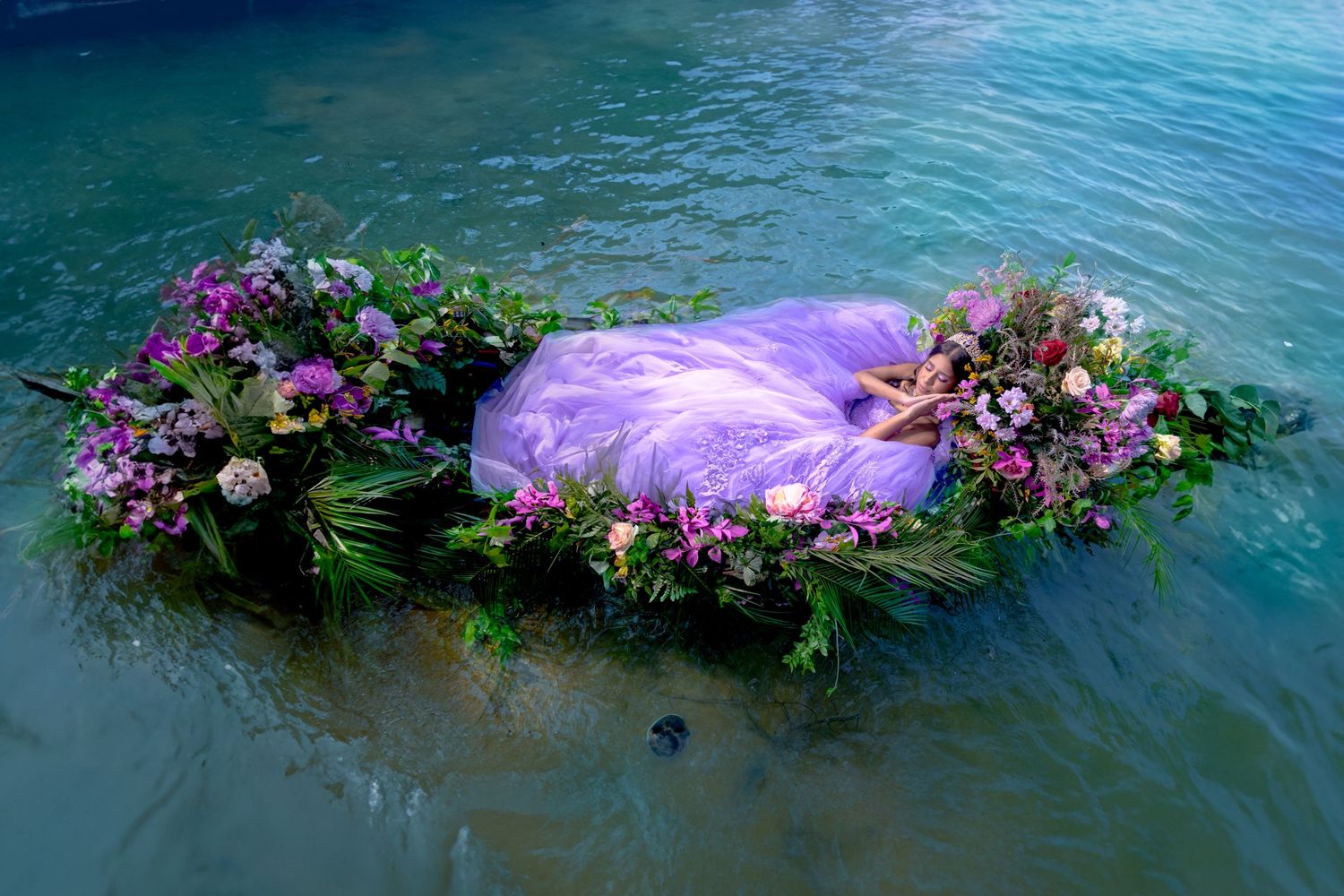 Floral garland floating on turquoise water with purple flowers creating an ethereal scene.