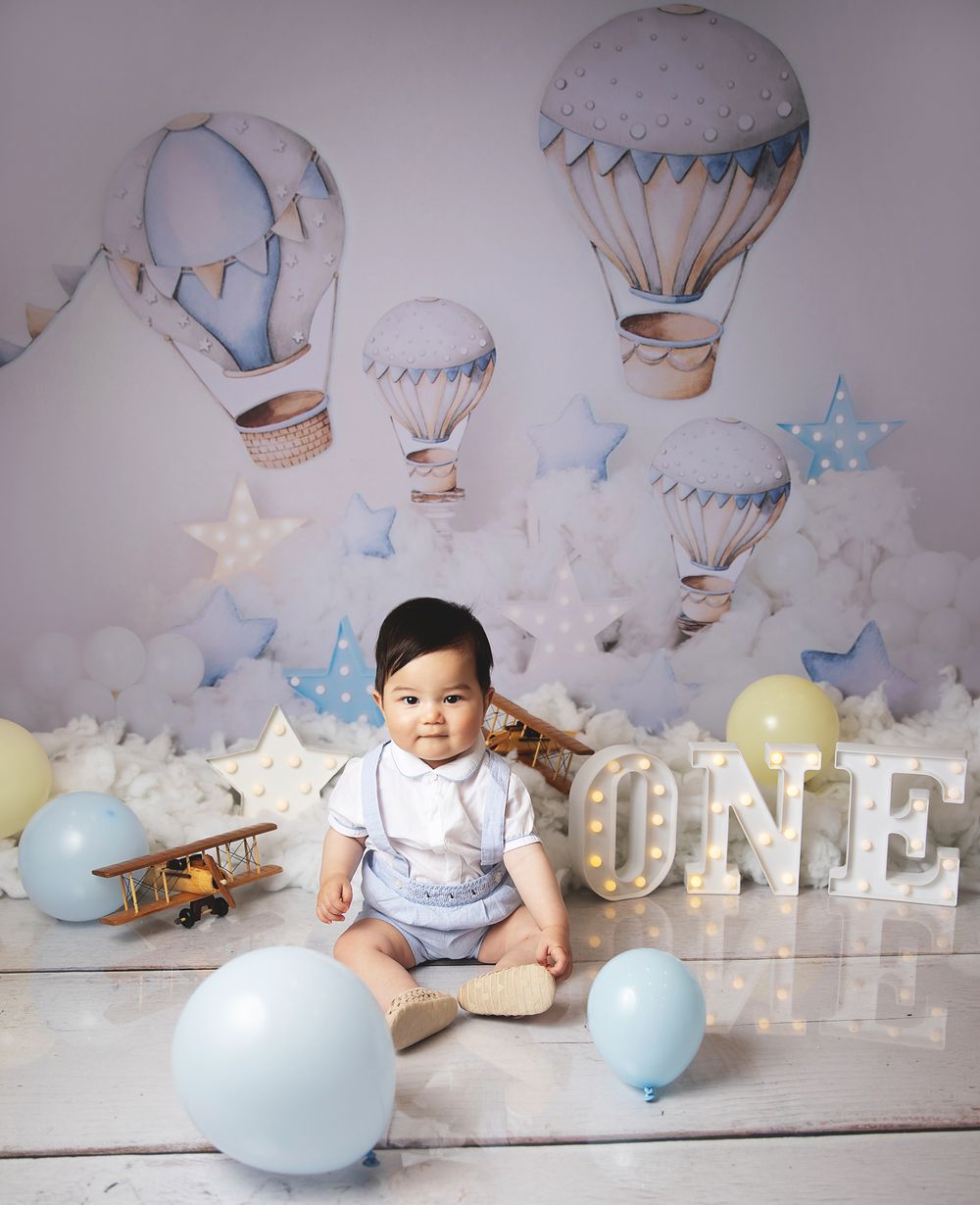 Hot air balloon themed first birthday photo setup with soft blue balloons, decorative stars and vintage airplane decor.