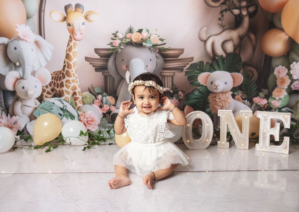 First birthday party setup with stuffed animals, floral decorations, 'ONE' letters, and soft pastel colors in nursery theme.