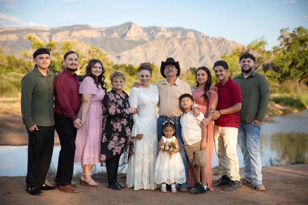 Family group photo outdoors with mountains backdrop, featuring adults and children dressed formally, celebrating an anniversary.