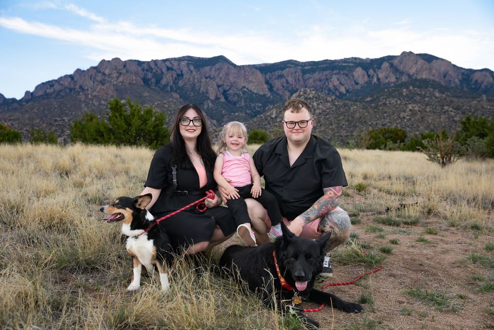 Family with toddler and two dogs posing in front of Sandia Mountains in New Mexico during golden hour.