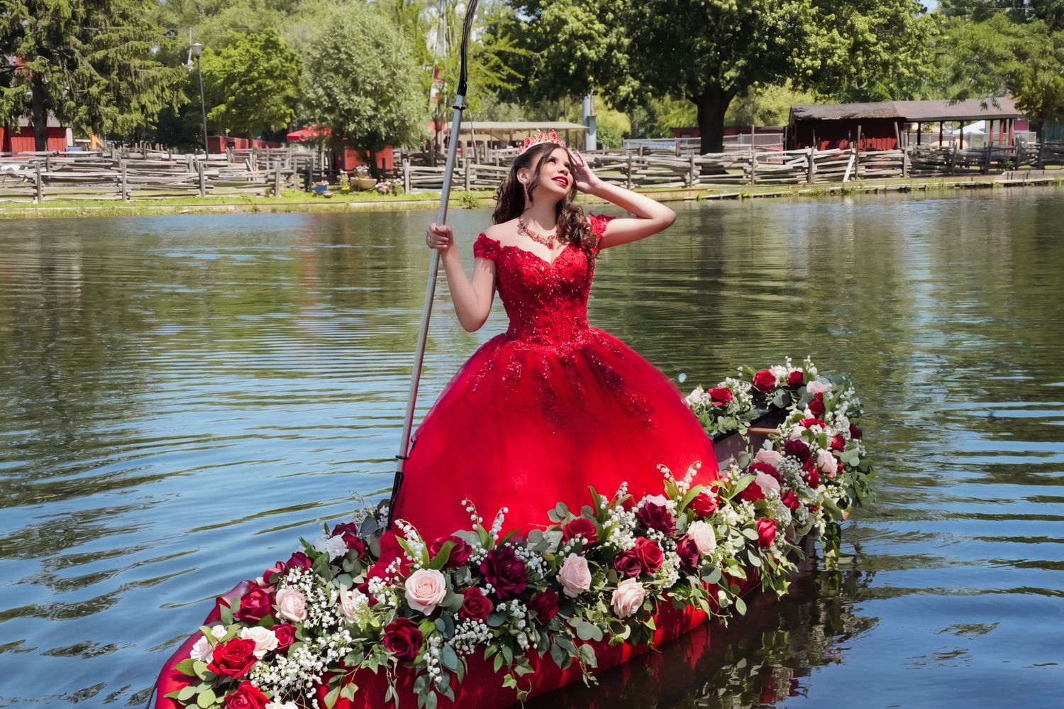 Young woman in red quinceañera gown rides a flower-adorned boat on a serene lake surrounded by lush greenery. Toronto GTA