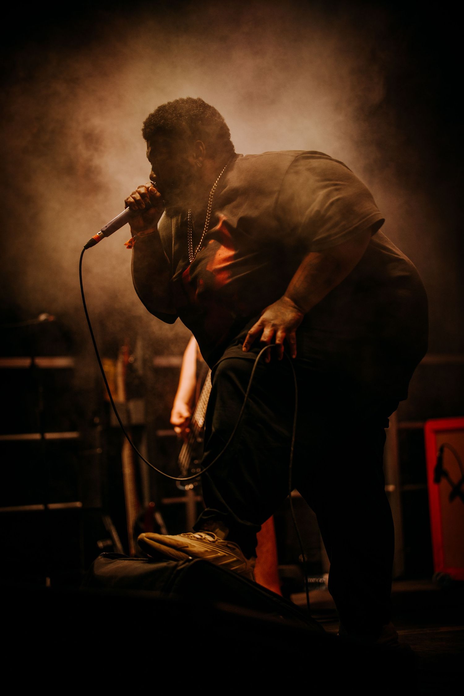 Musicians perform energetically on stage during a live rock concert with dramatic lighting and smoky atmosphere.