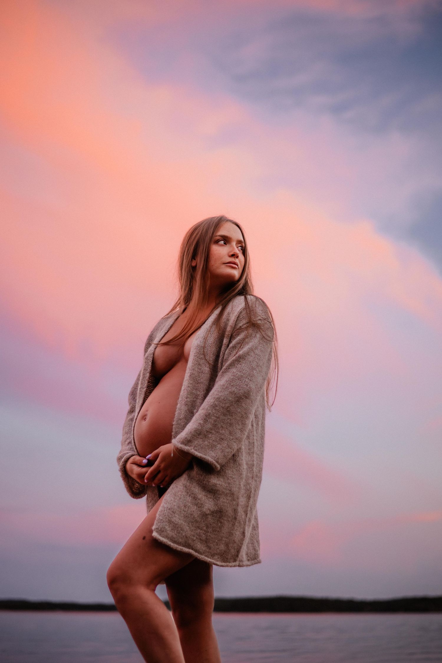 En gravid med bar mage under rosa himmel vid havet