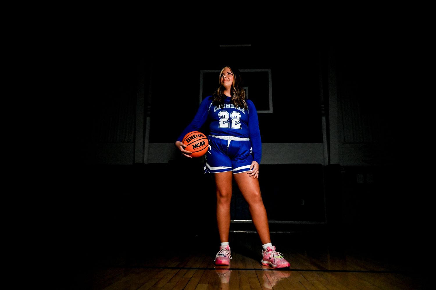 Basketball player poses in blue jersey number 22 on dark court with dramatic lighting.