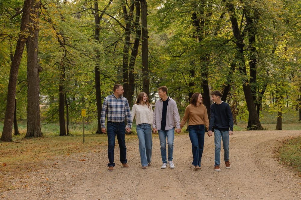 Family of five walking together on a dirt path through an autumn forest with colorful foliage.