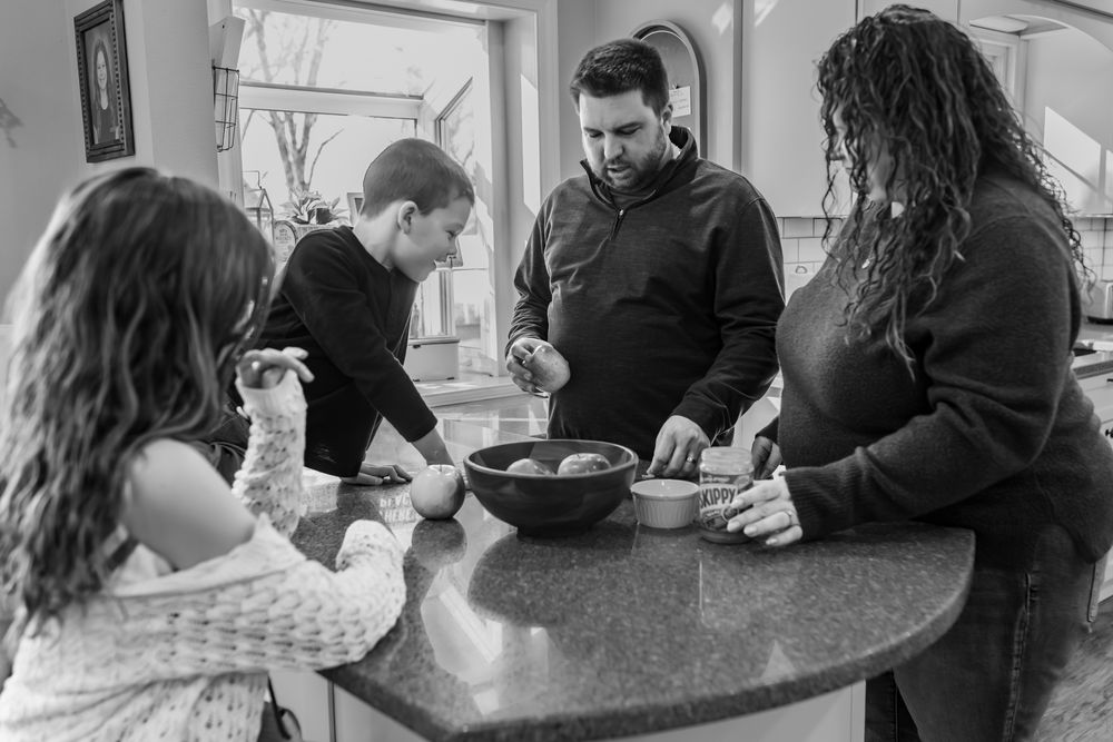 Black and white photo of a family preparing food together at a kitchen counter.