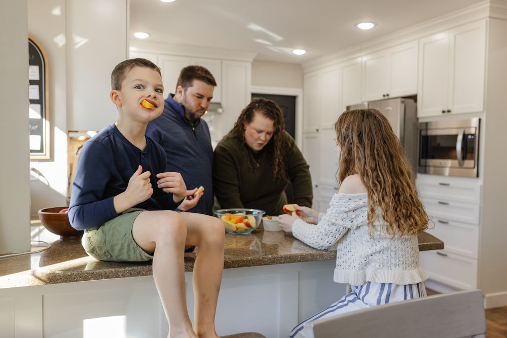 Family enjoying healthy snacks together in a modern white kitchen, with children sitting on the counter.