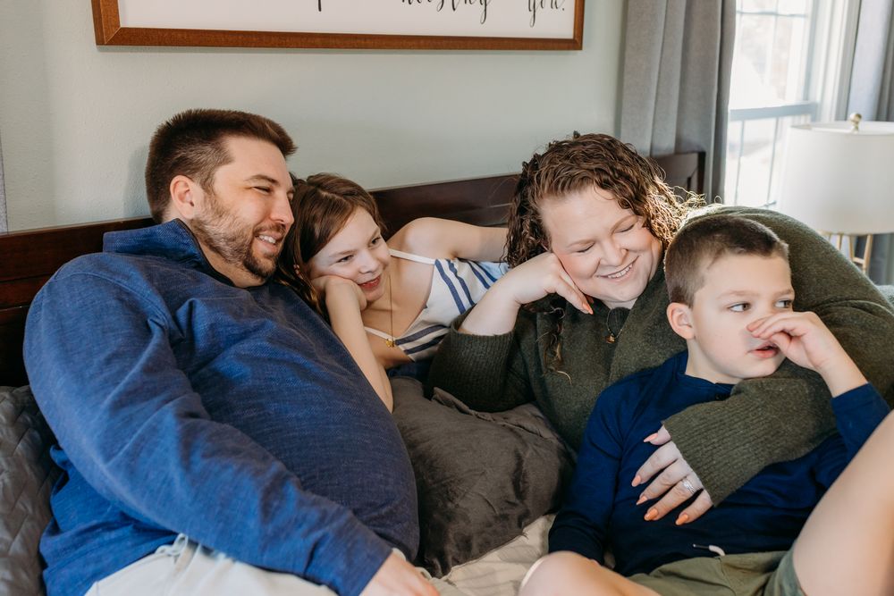 Happy family of four laughing together on a cozy bed, parents and two children enjoying a fun moment.