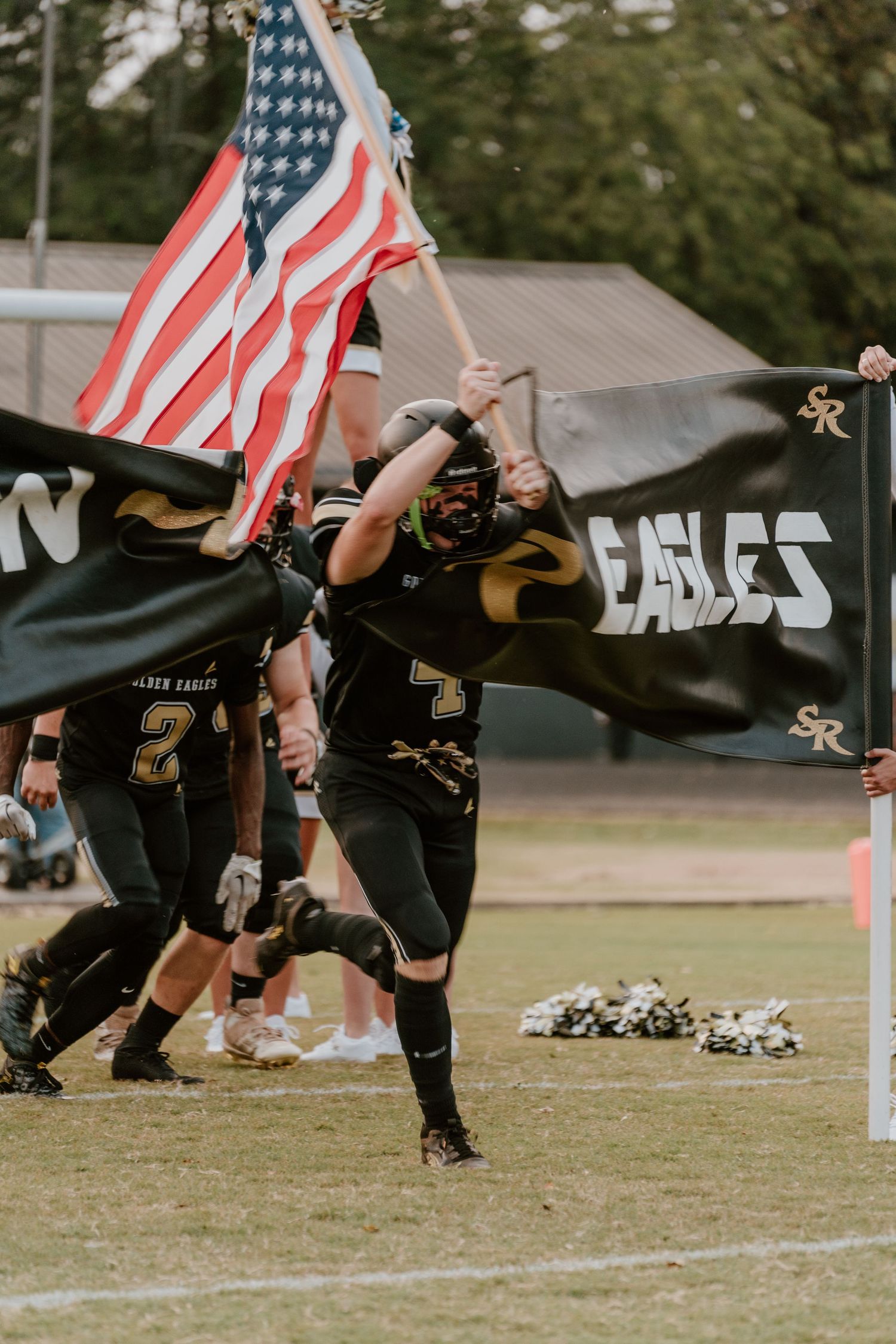 Athletes carrying American flags running across sports field during game event.