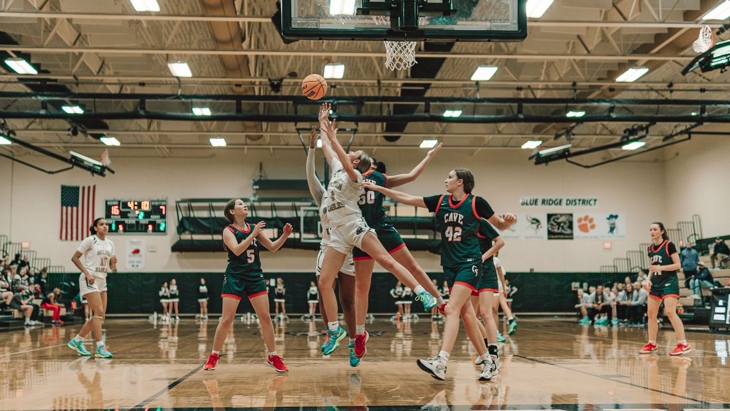 Basketball players jump for the ball during intense indoor game action.