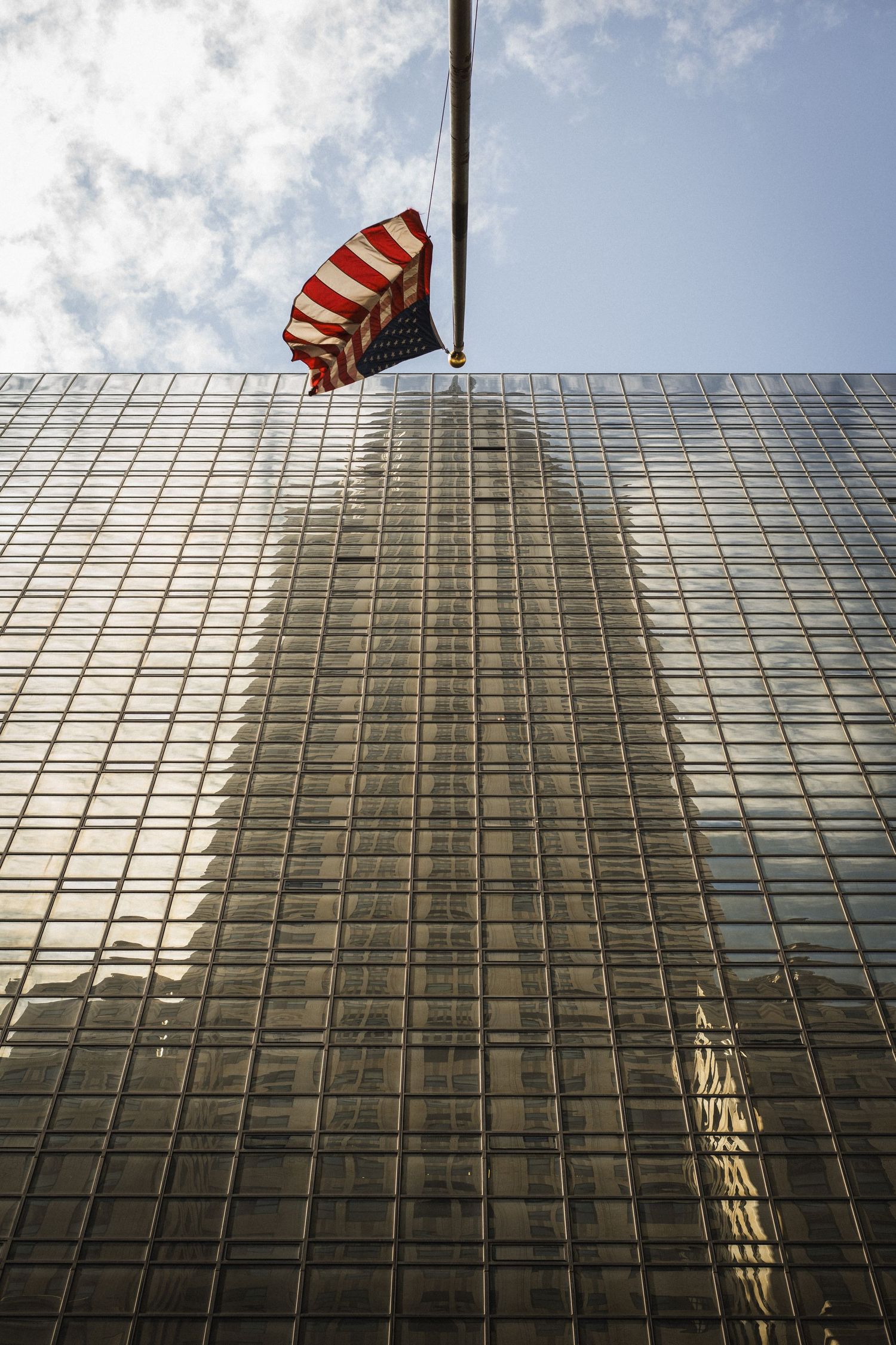 Photo du reflet du Chrysler Building à Manhattan, New-York, dans une façade vitrée d'un immeuble en face. Le drapeau Américain apparaît