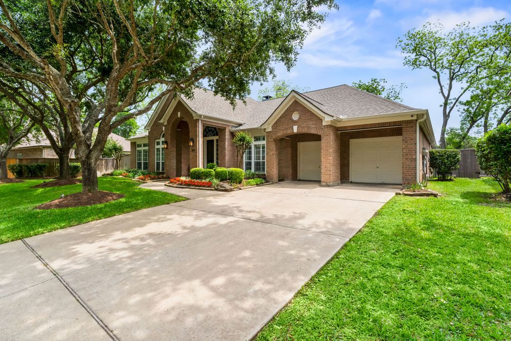 Large brick ranch home with attached garage and beautiful landscaping under mature oak trees.