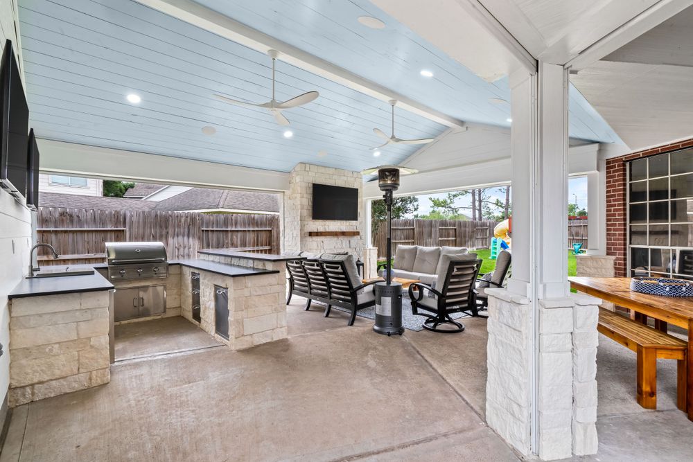 Covered outdoor kitchen and living area with stone counters and comfortable seating arrangement.