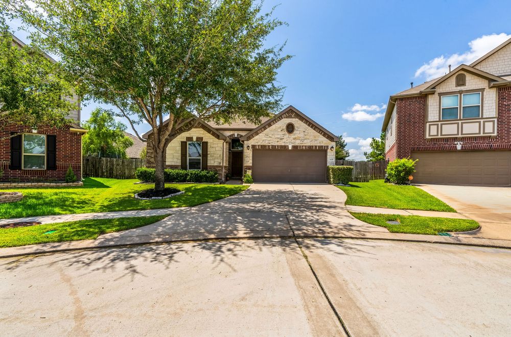 Panoramic view of suburban houses with well-maintained lawns and driveways on a sunny day with blue skies.