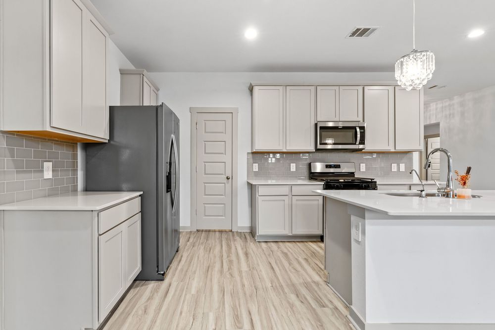 Modern white kitchen renovation with light wood flooring, stainless steel appliances and crystal pendant lighting.
