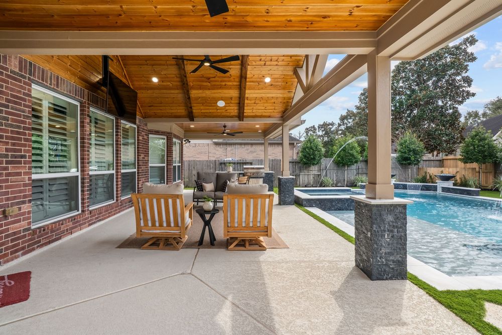 Covered patio with ceiling fans, wooden chairs, and a sparkling pool in a beautifully landscaped backyard.