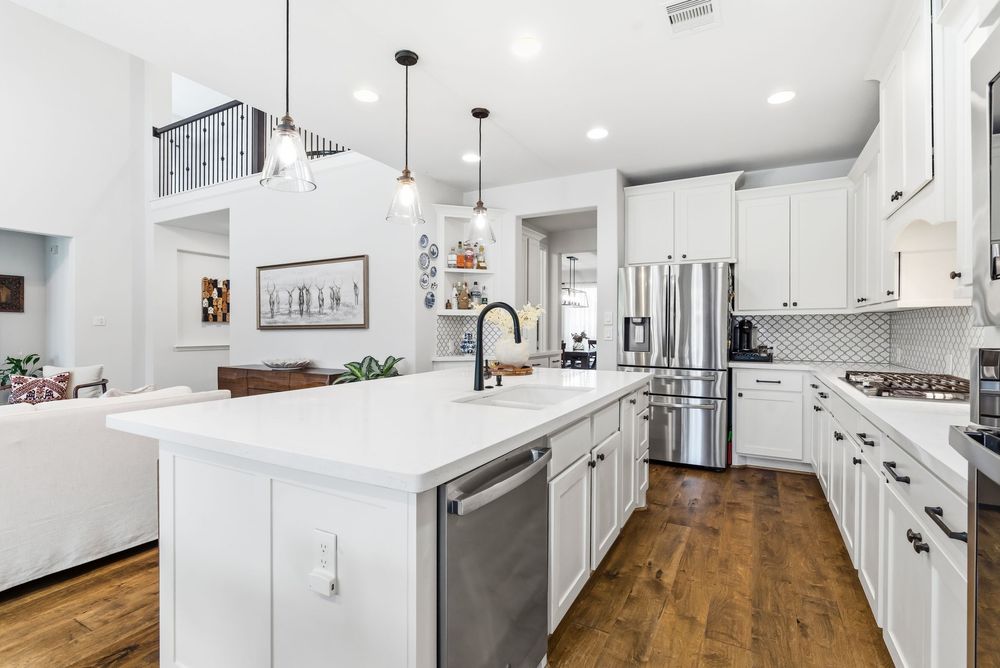 Modern white kitchen with island, pendant lights, stainless steel appliances, quartz countertops, and hardwood floors.