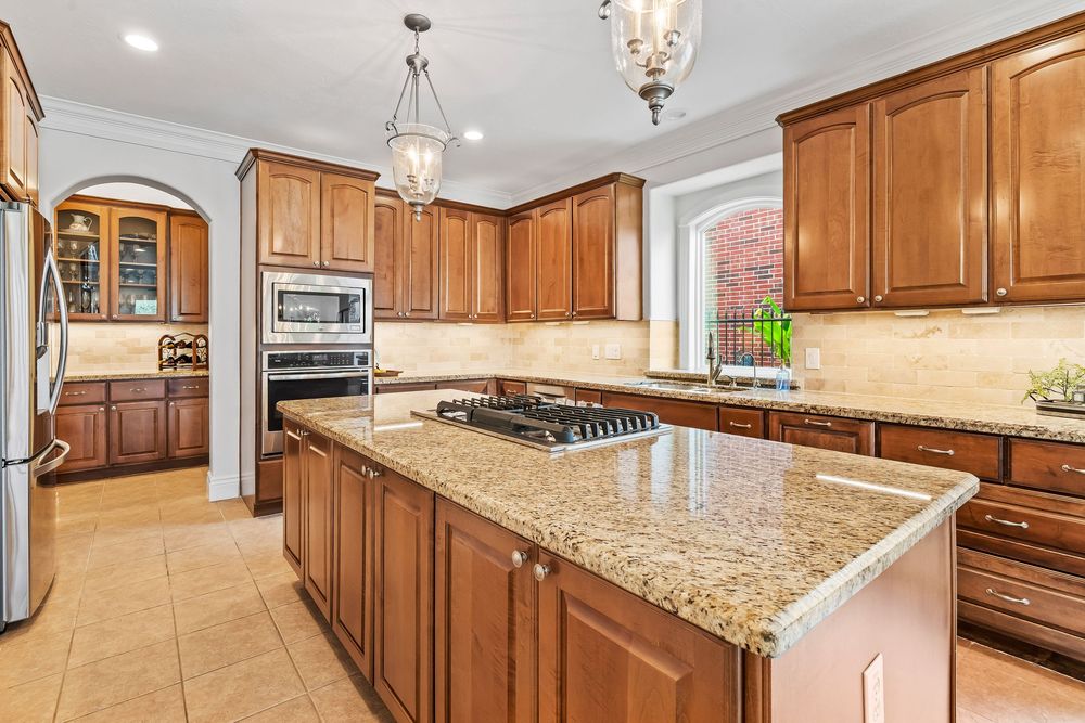 Spacious luxury kitchen with warm wood cabinets, granite countertops, pendant lights, and stainless steel appliances.