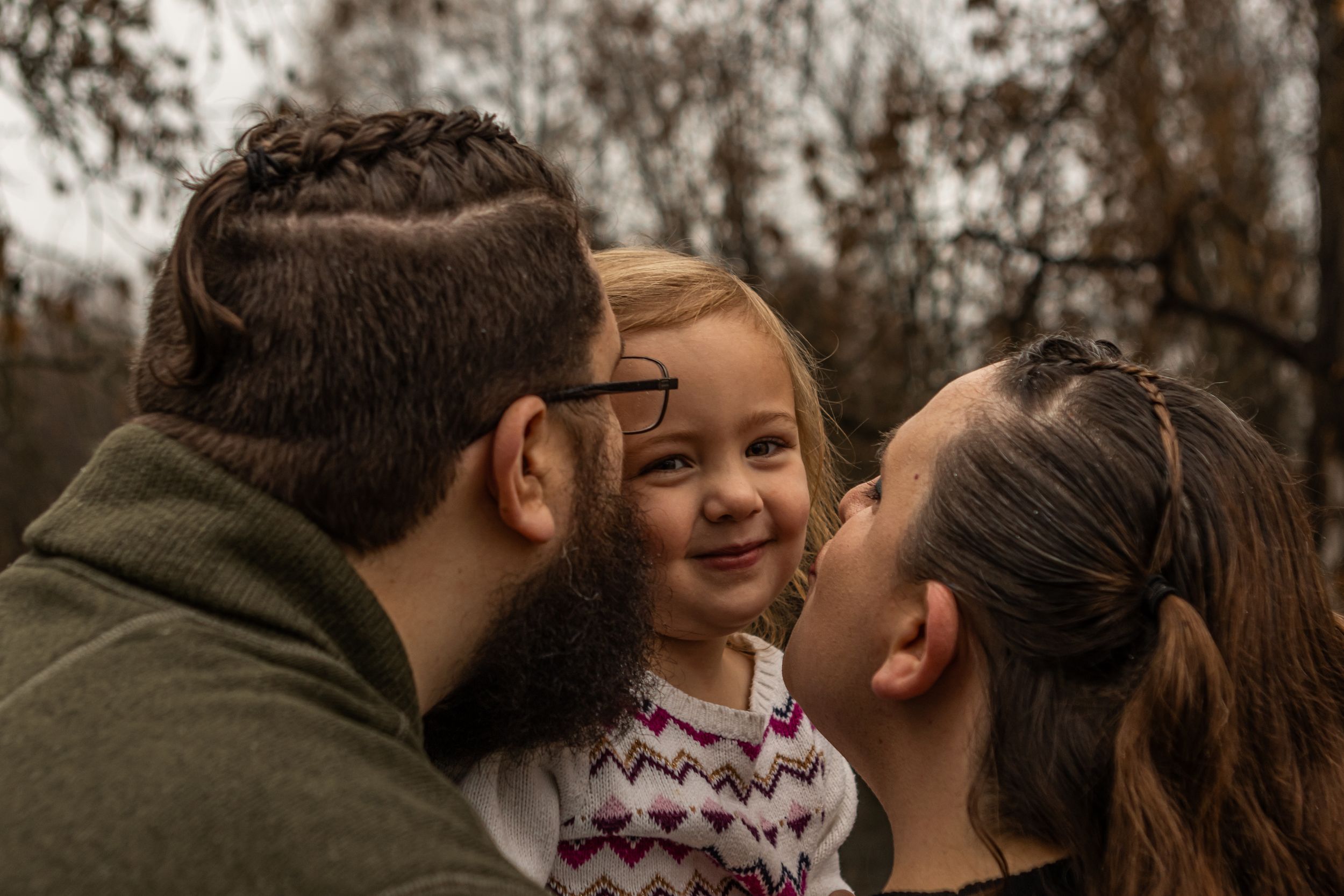 A couple kisses their toddler as she stares into the camera