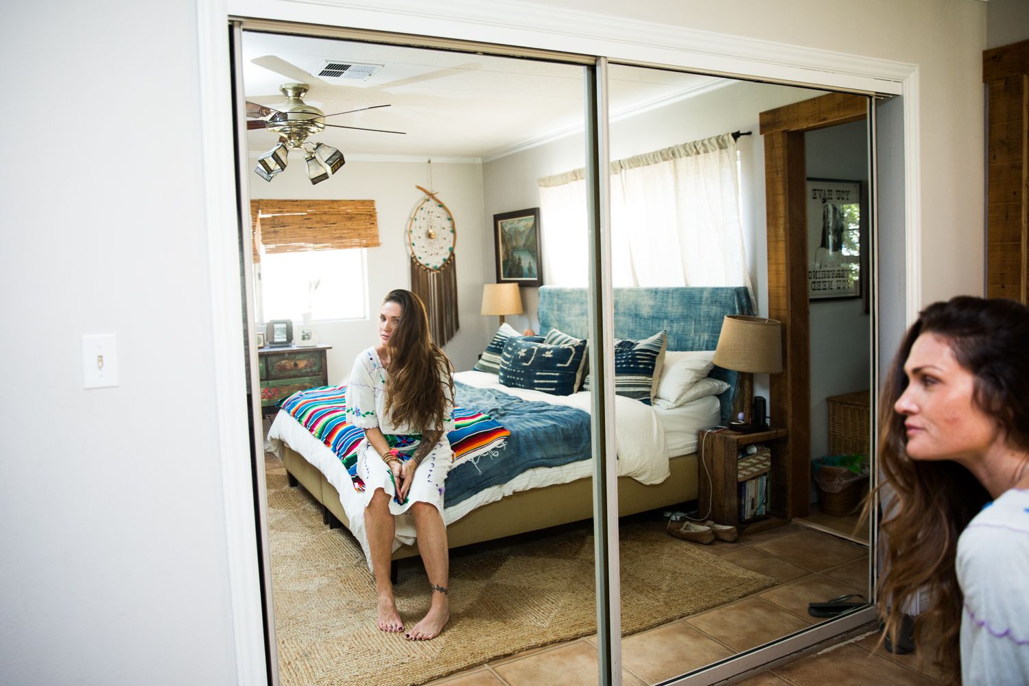 Woman viewing her reflection in large mirrored closet doors in a cozy bedroom with colorful bedding.