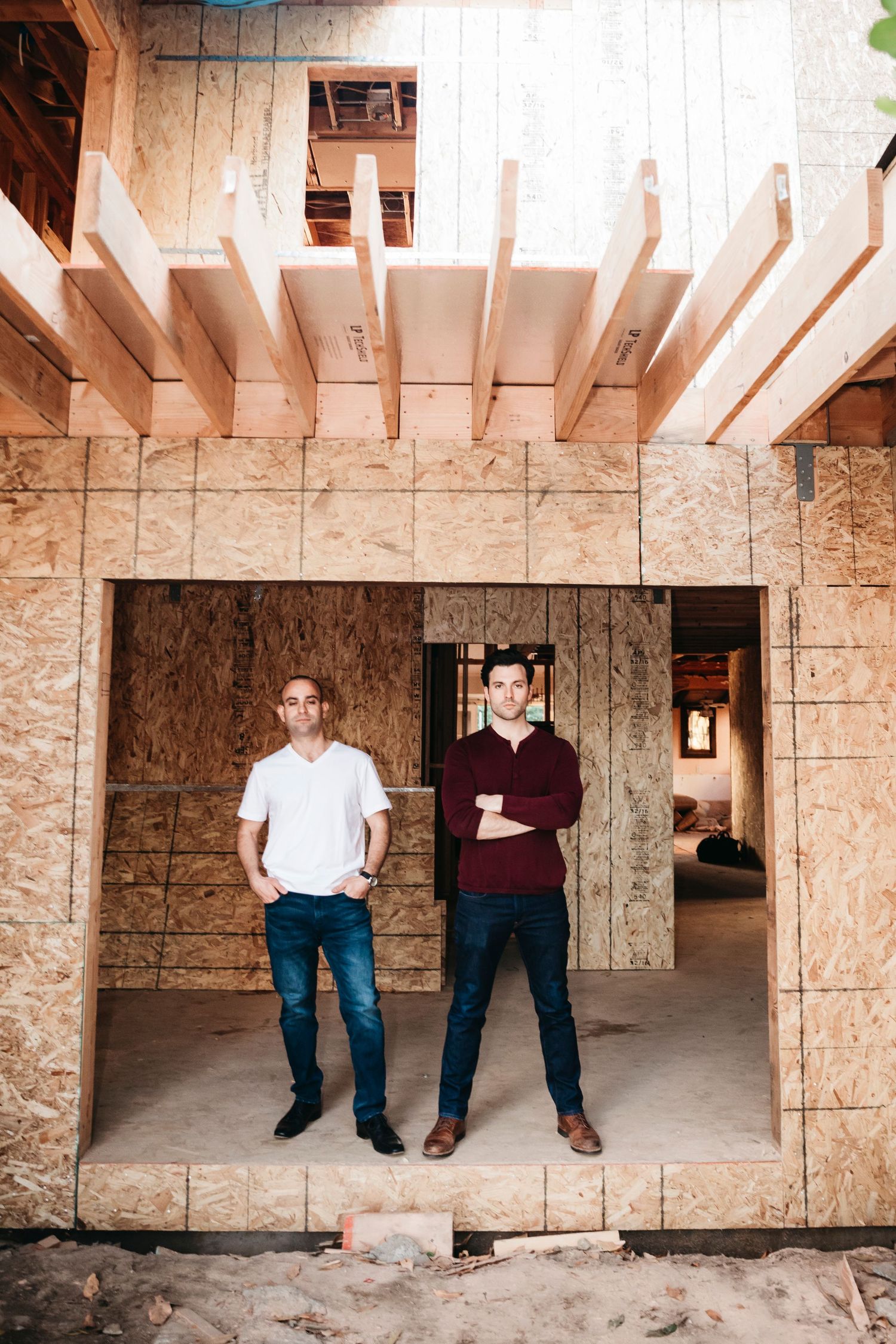 Two men standing in the framed doorway of a house under construction with exposed OSB walls and wooden joists.