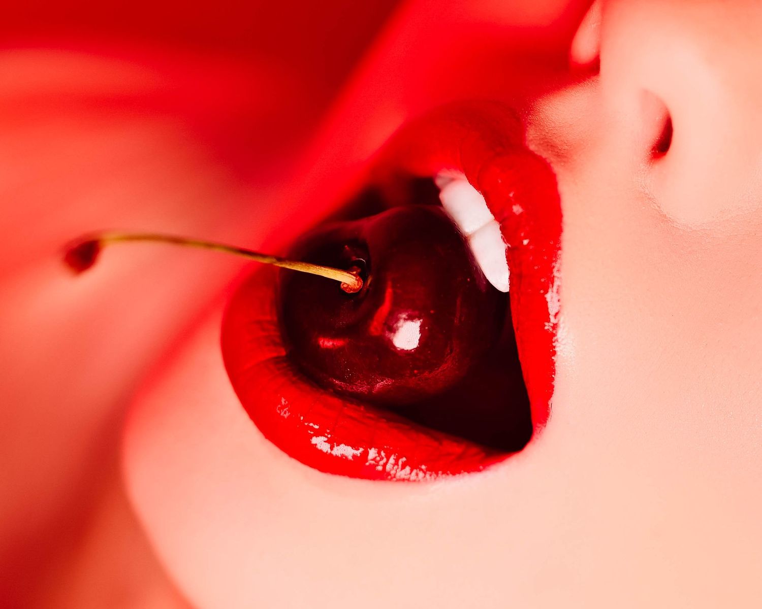 Close up artistic photo of bright red lips with a dark cherry against vibrant red background.