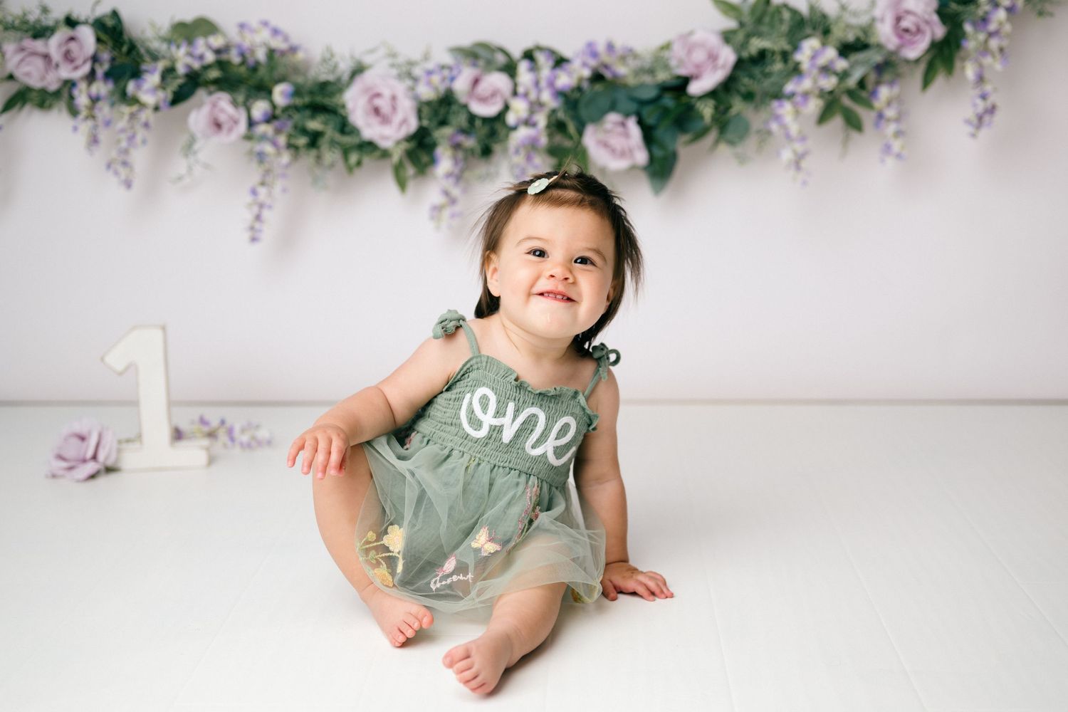 Floral garland with pink roses and greenery hangs against a white wall creating an elegant backdrop for photography.