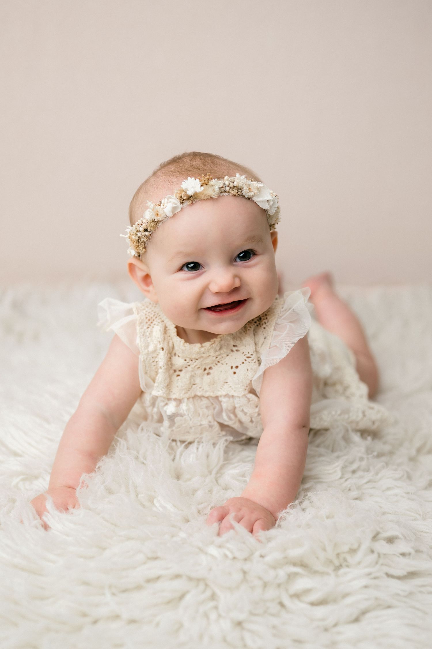 Baby wearing white lace dress and floral headband lies on soft white blanket in three similar studio portraits.