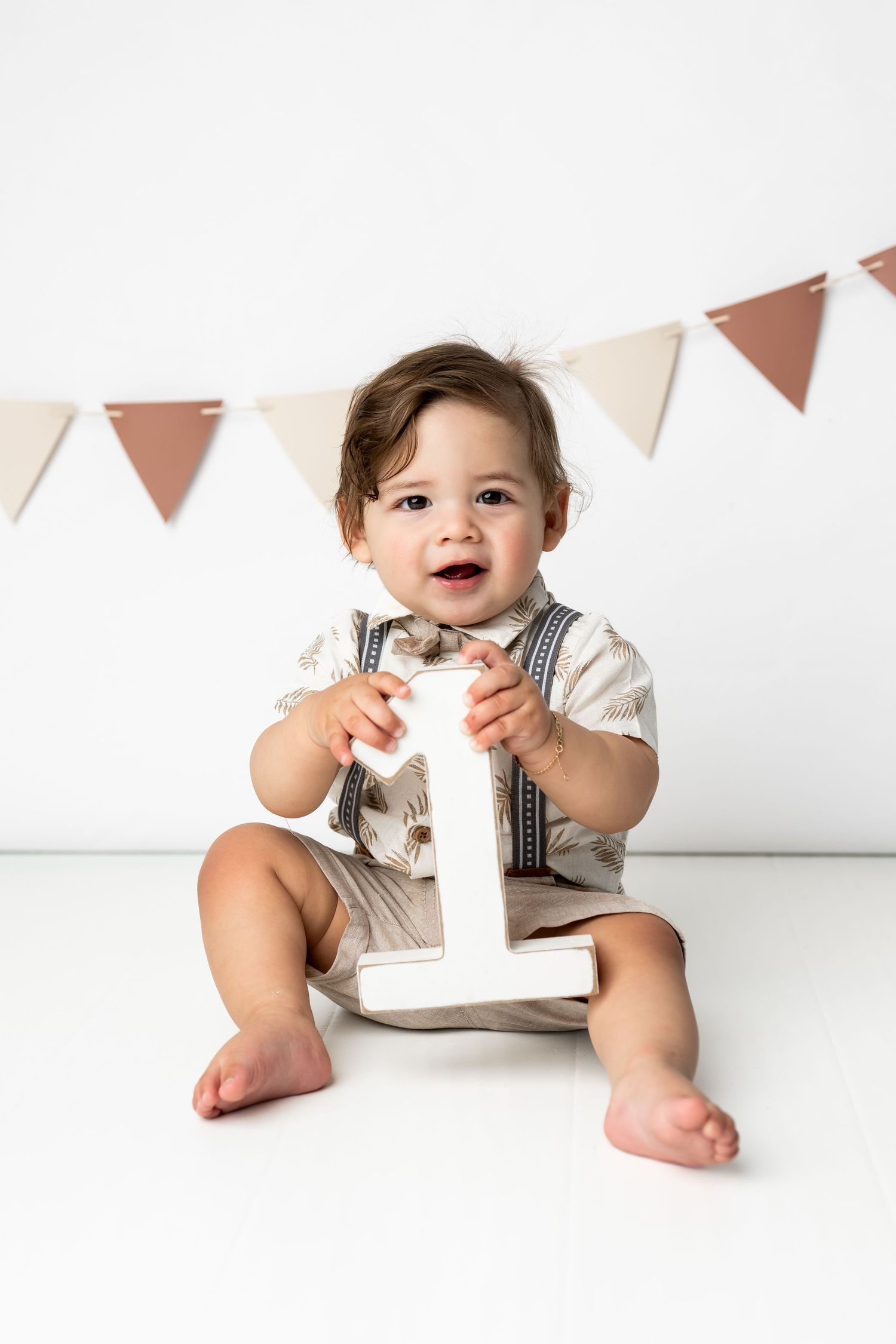 Small child wearing suspenders and formal attire holds number one decoration against white background with triangle banner.