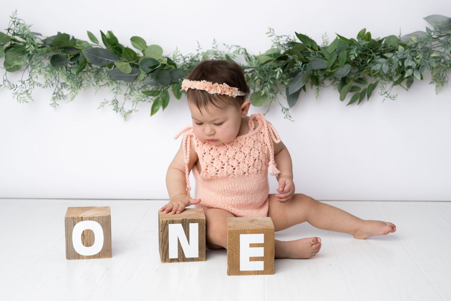A collection of wooden letter blocks and greenery decorations arranged for a first birthday celebration photoshoot.