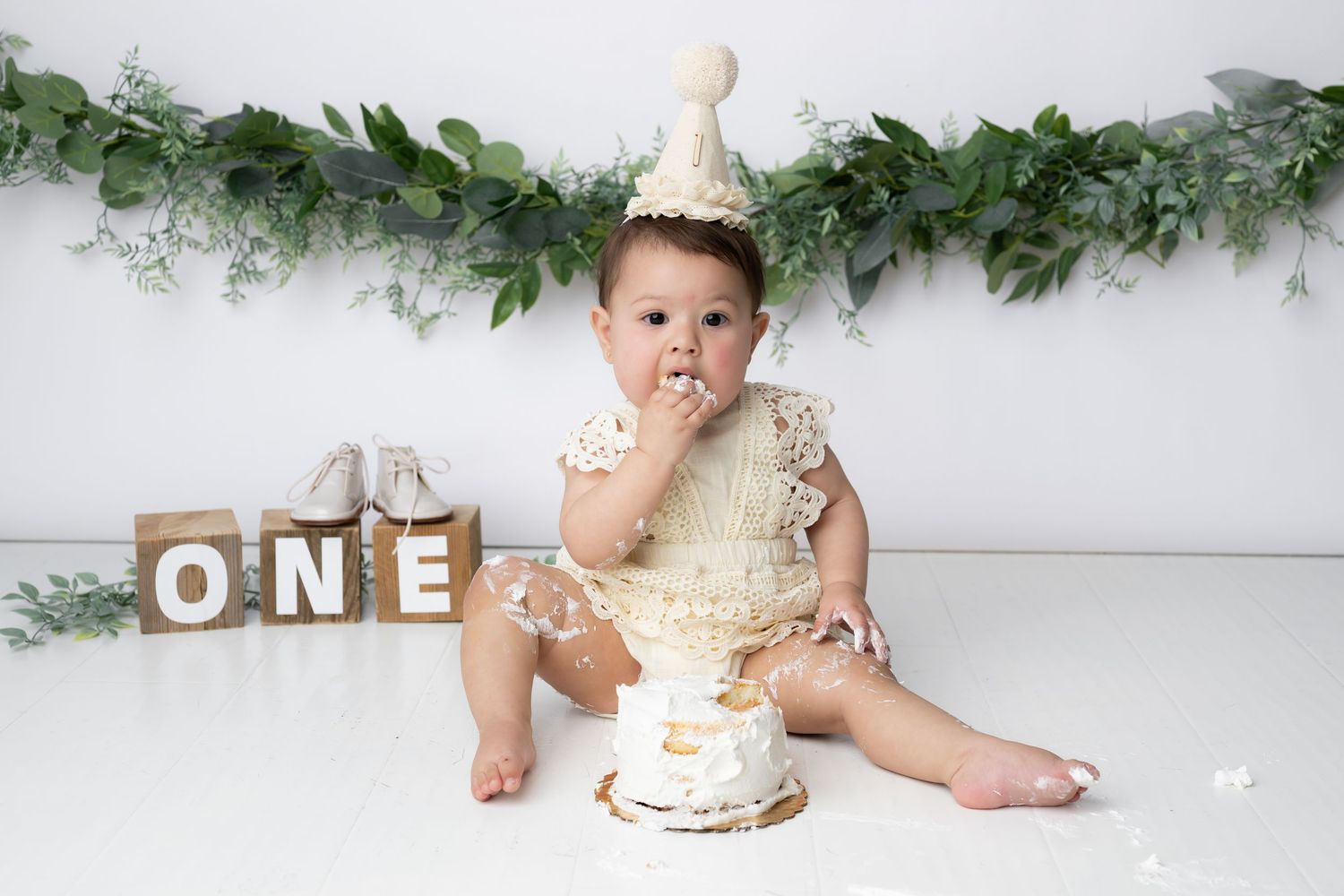 First birthday cake smash photo session with wooden blocks spelling ONE and eucalyptus garland decoration.