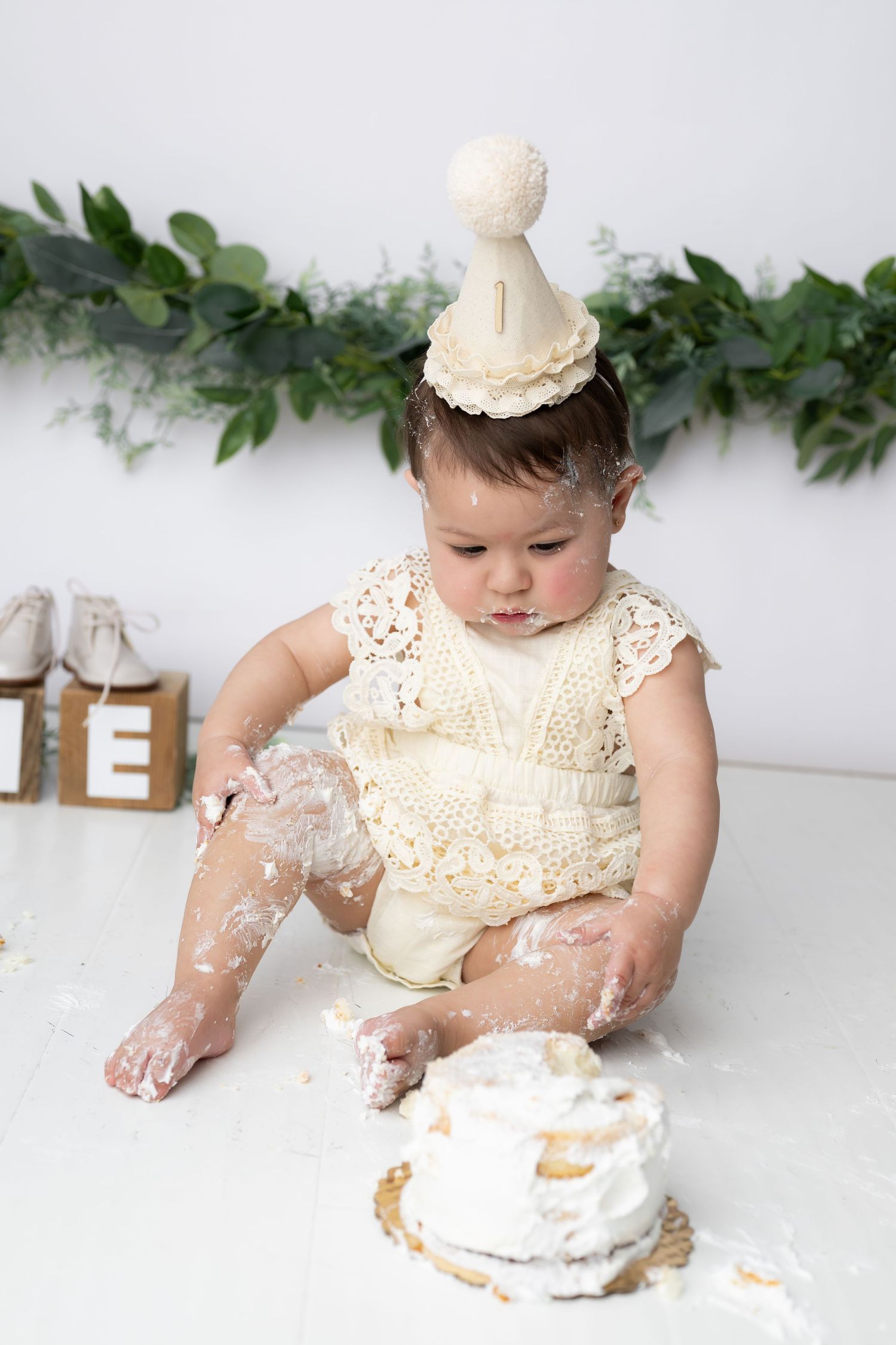 Baby playing with cake and frosting during first birthday cake smash photoshoot with leafy decor.