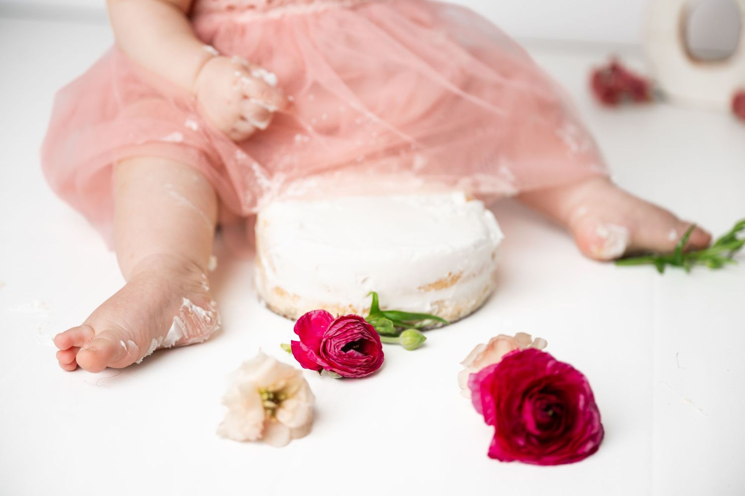 White cake setup with red roses and pink tulle dress details for cake smash photography session.