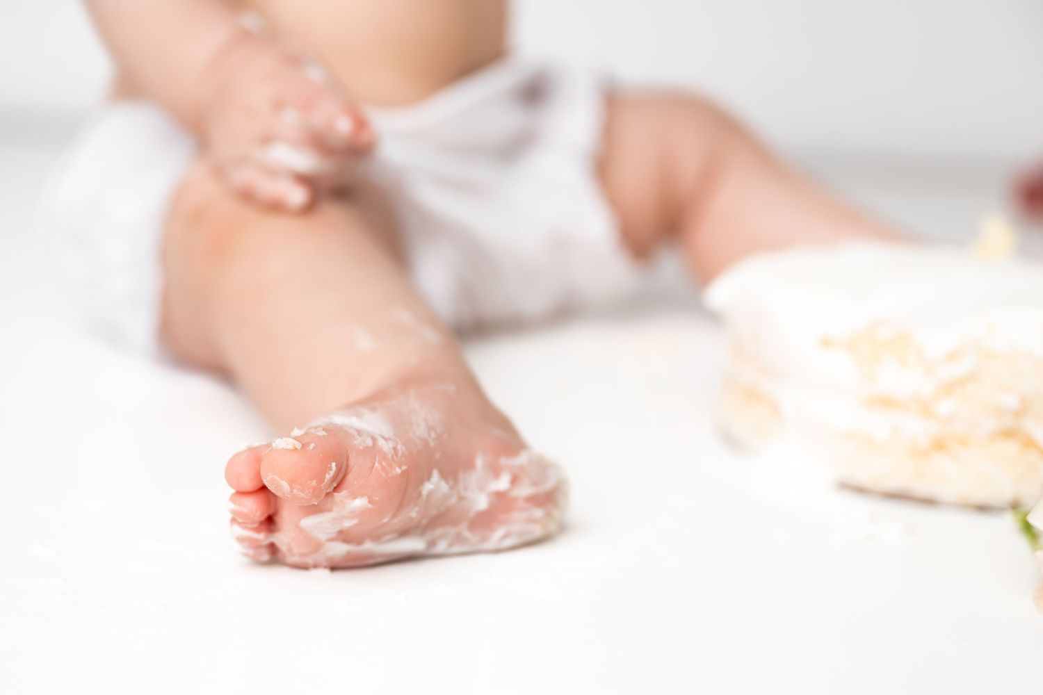 Baby's tiny hands covered in flour or baking powder while playing during cooking time on white surface.