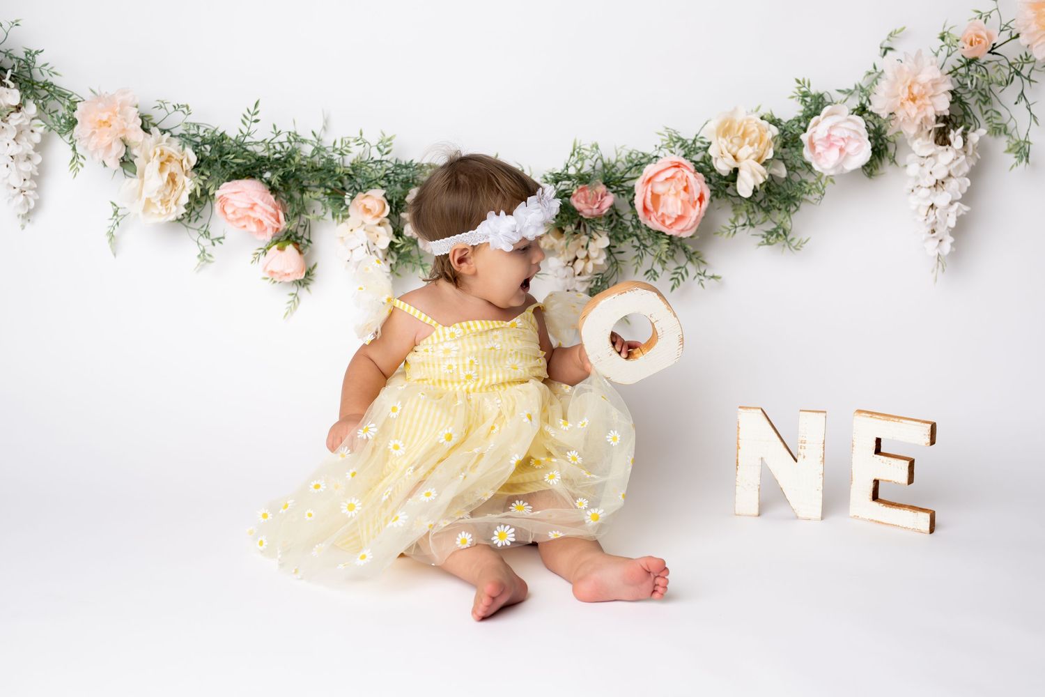 A spring-themed first birthday setup with floral garland and 'ONE' letters.