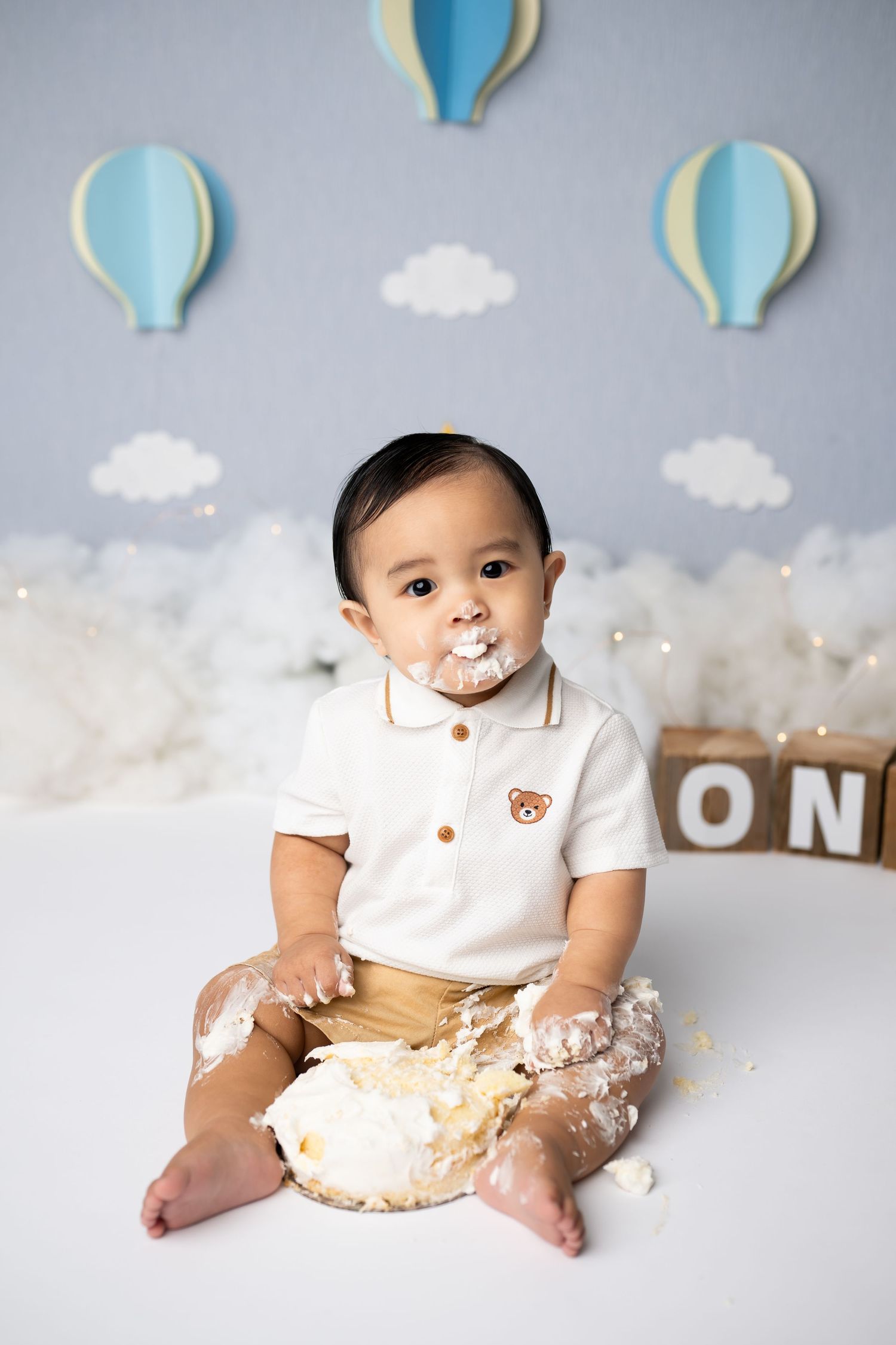 Cake smash first birthday photo with white and blue hot air balloon themed backdrop.
