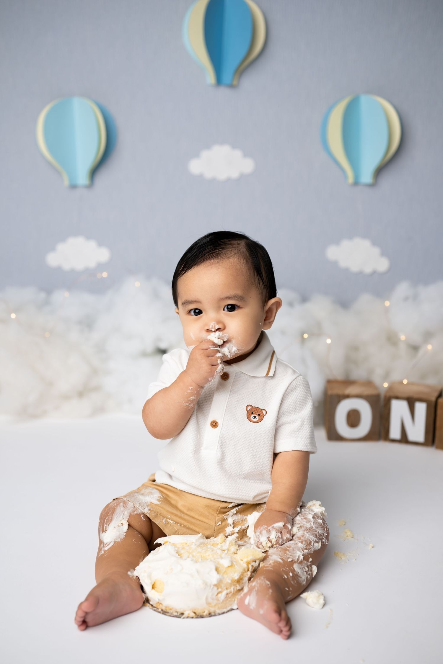 First birthday cake smash session in progress with festive cloud and balloon backdrop.