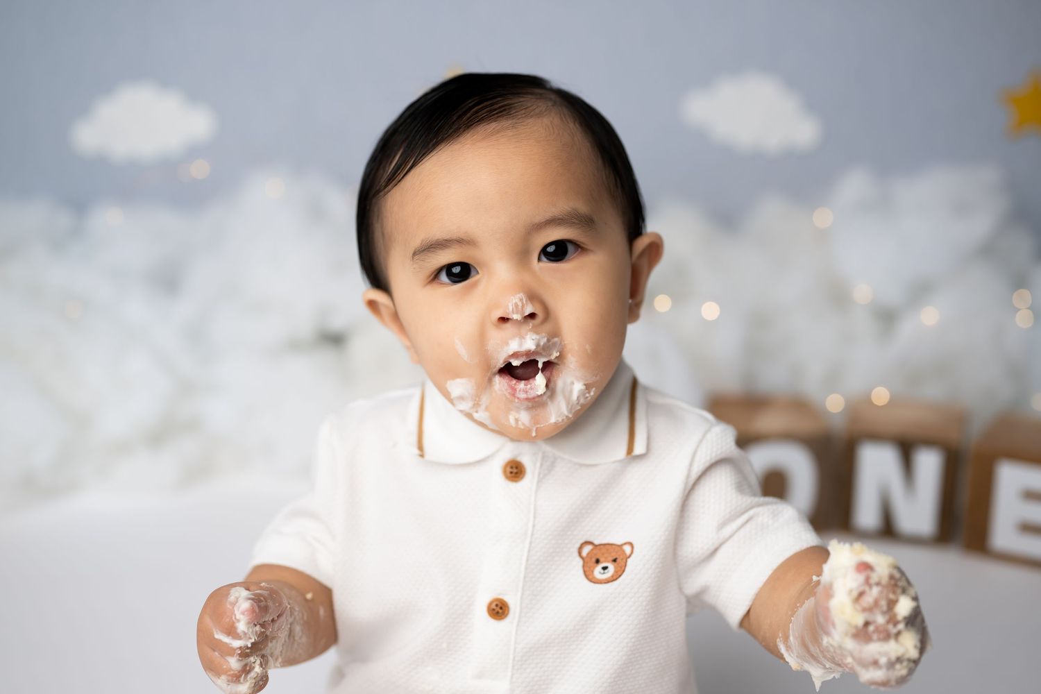 Joyful cake smash portrait with cream frosting and balloon themed background.