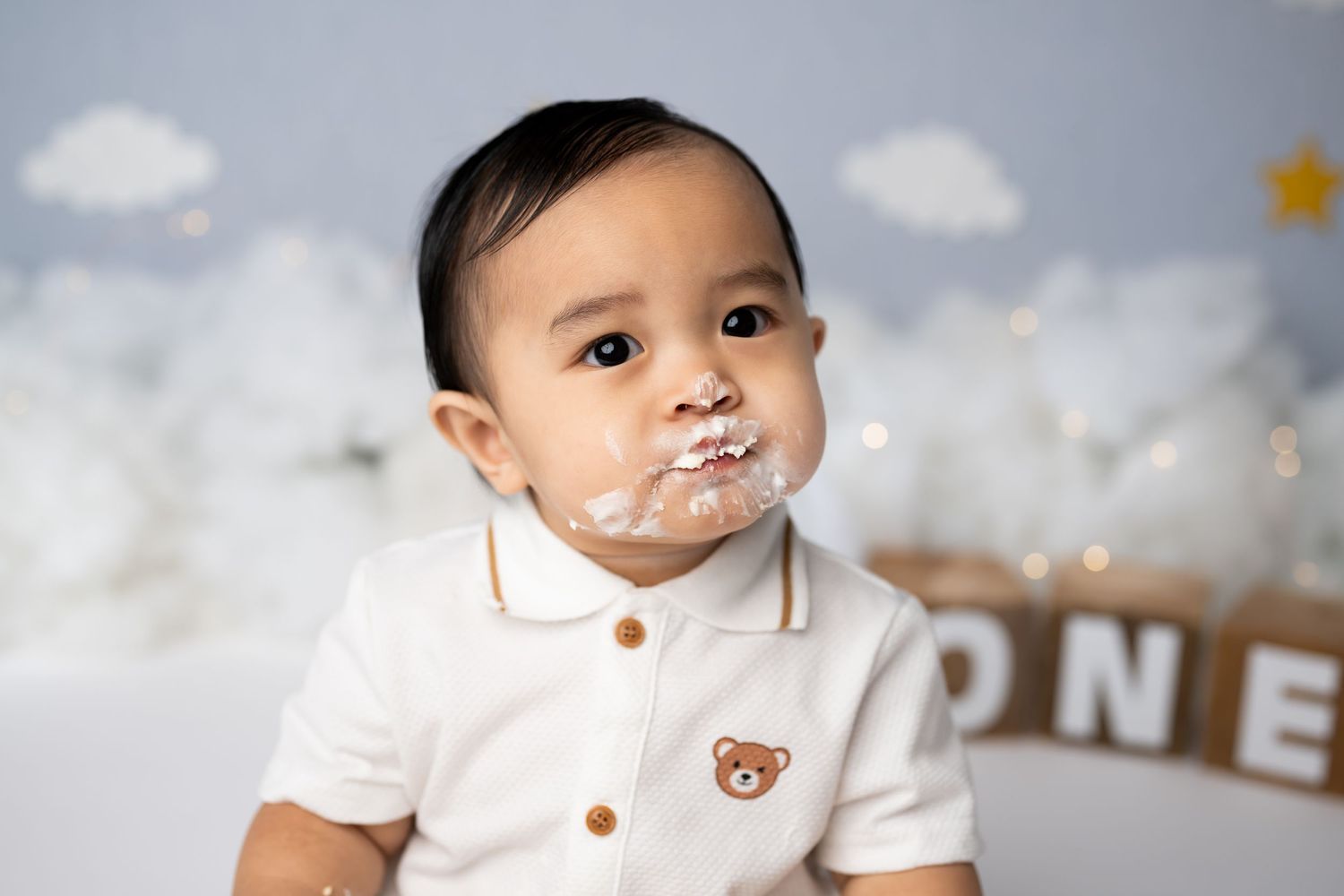 Messy cake smash closeup with white frosting and decorative balloon backdrop.