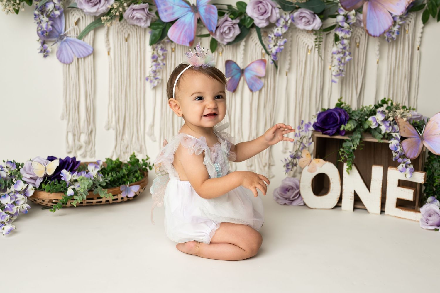 A festive first birthday setup with floral decorations, butterflies and 'ONE' signage.