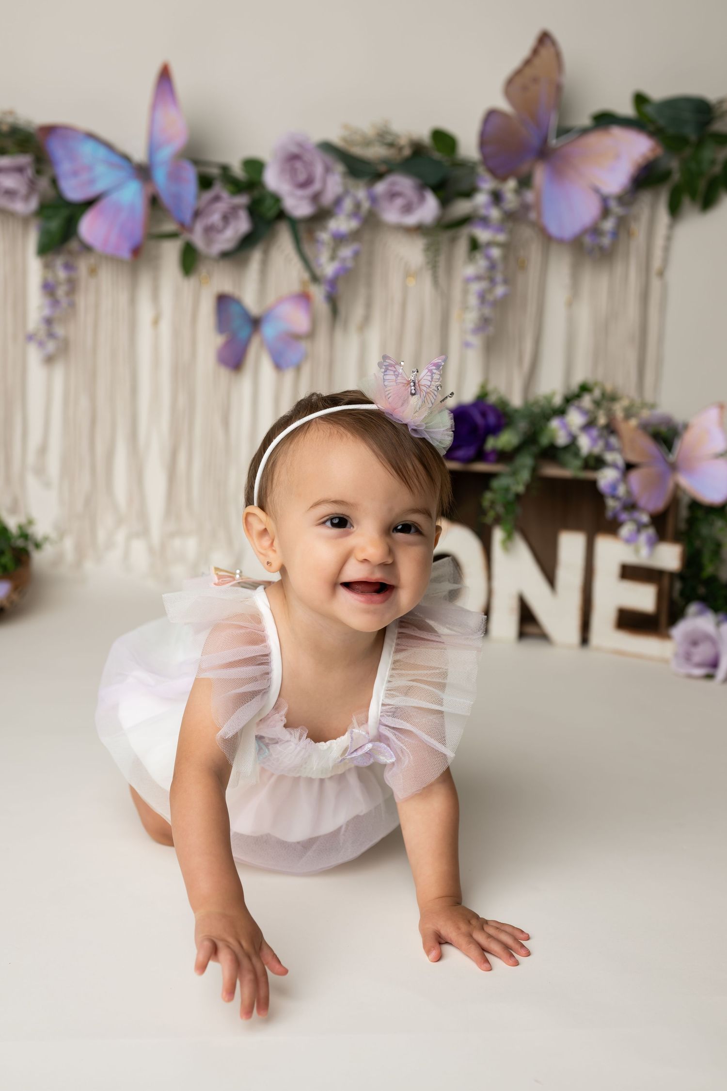 A joyful first birthday portrait with butterflies and purple floral decorations.