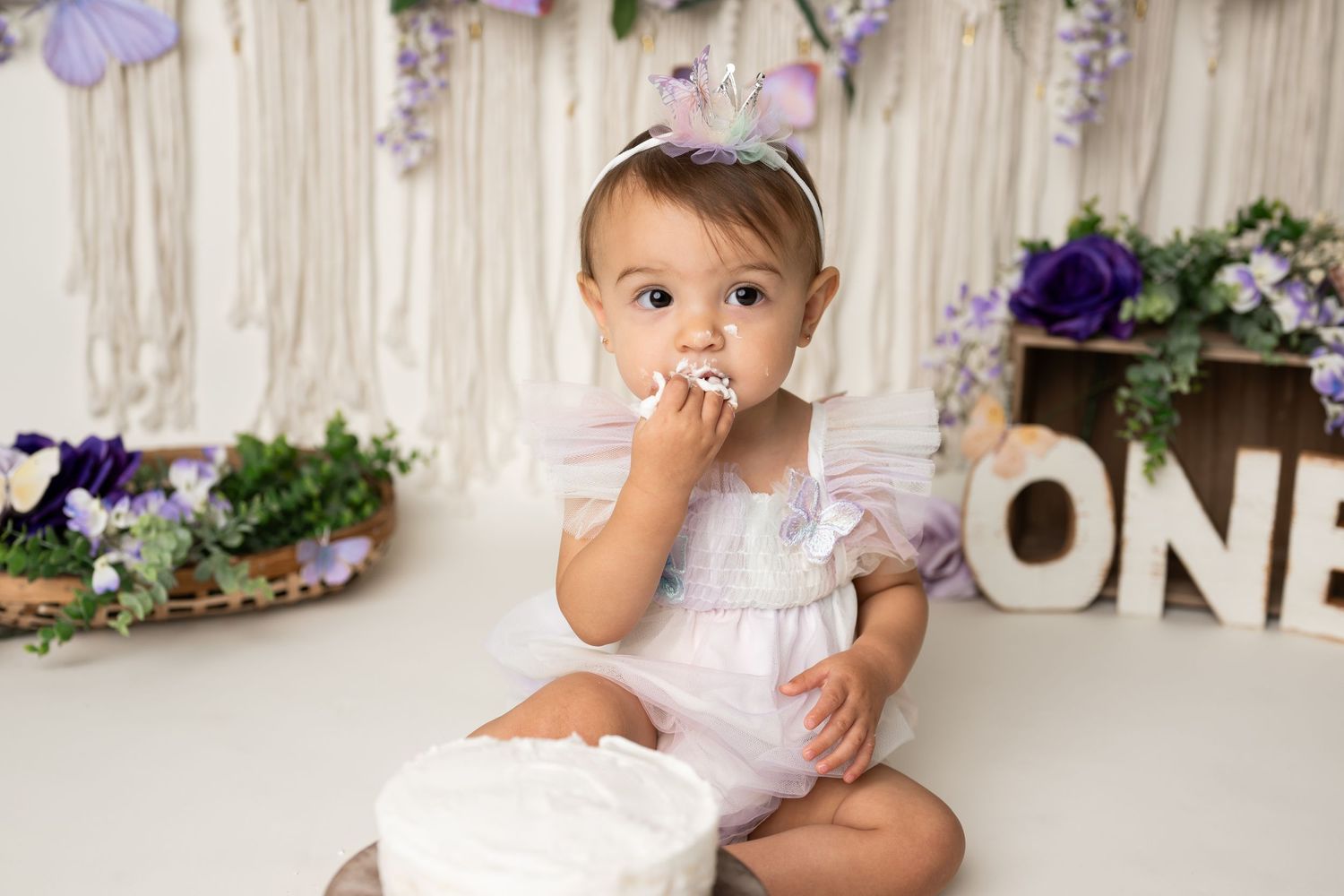 A sweet cake smash session with white dress and butterfly themed decorations.