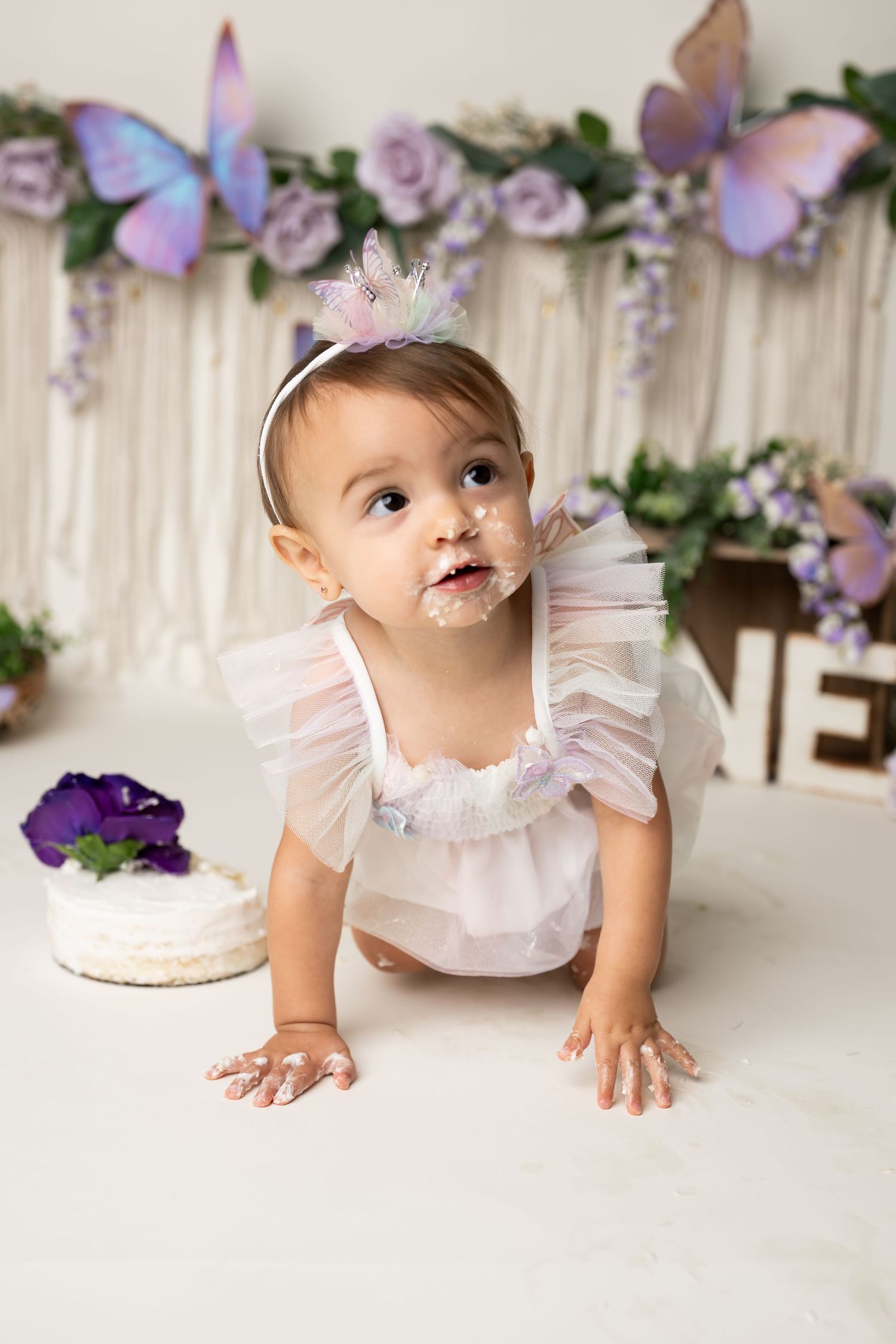 A playful cake smash moment with frosting and butterfly decorations.