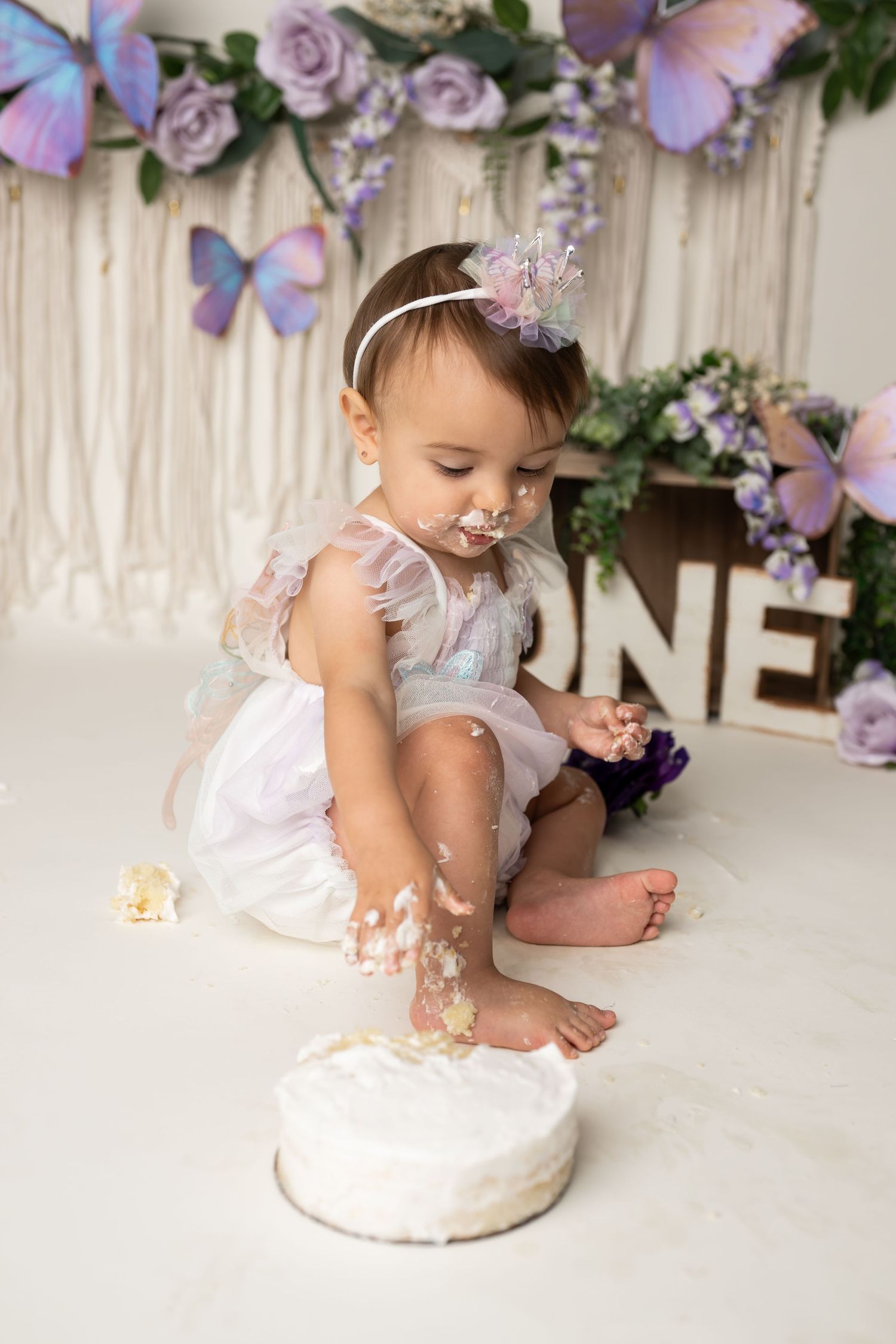 A first birthday cake smash with white cake and purple butterfly decorations.