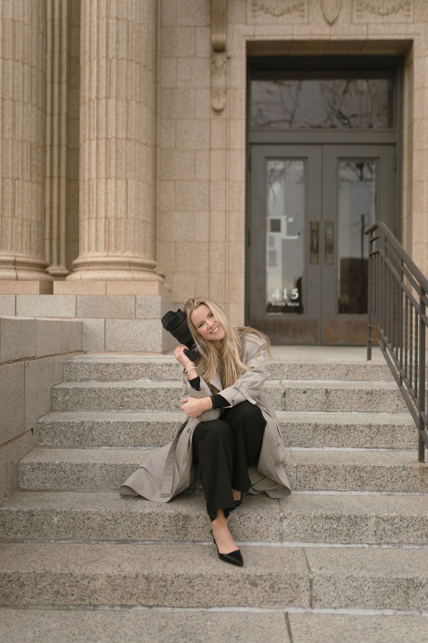 A photographer in casual attire sitting on a green chair holding a professional camera.