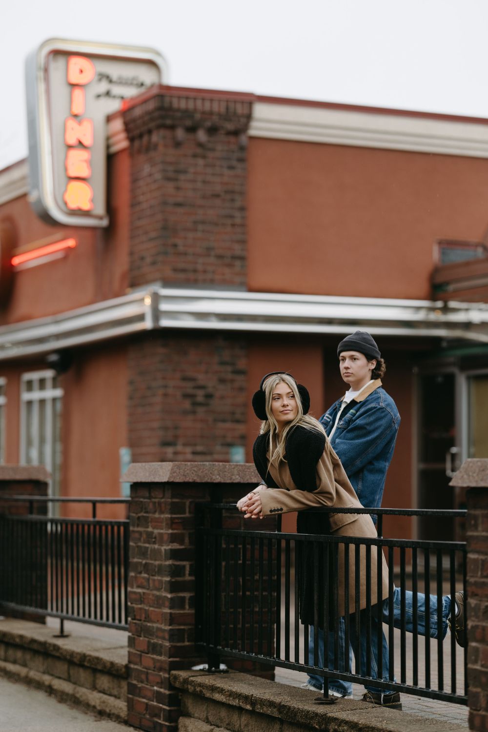 A couple stands on a brick building's balcony looking out into the distance.