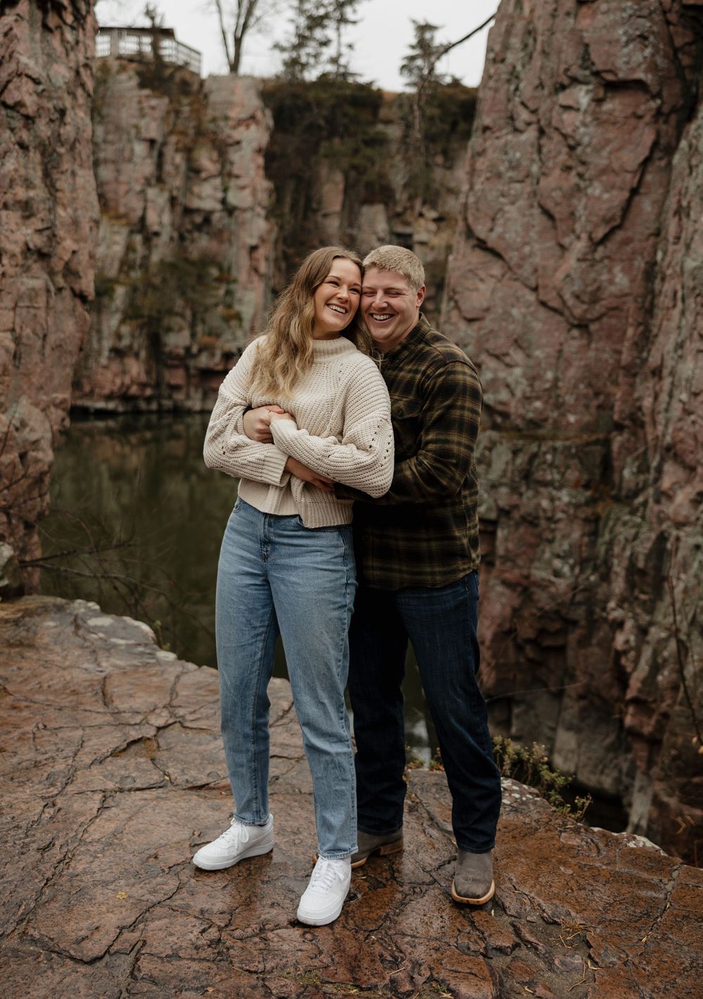 Romantic couple embracing at a scenic quarry with dramatic rock formations and water.