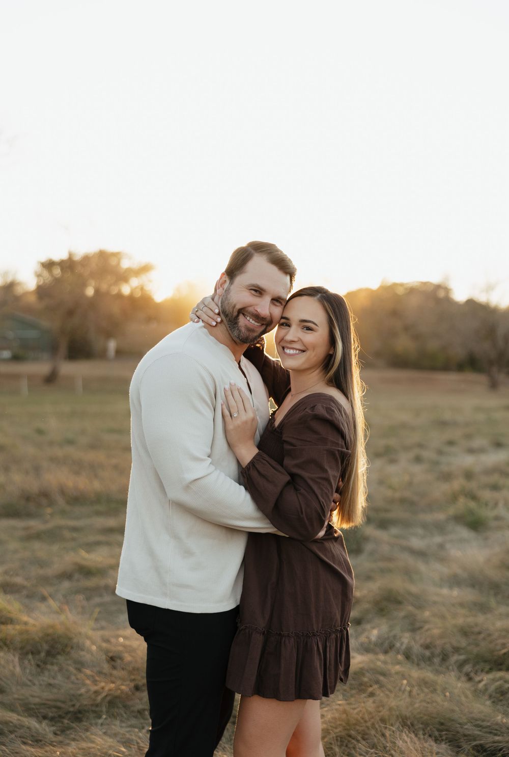 Couple embracing in a field during sunset wearing casual sweaters.