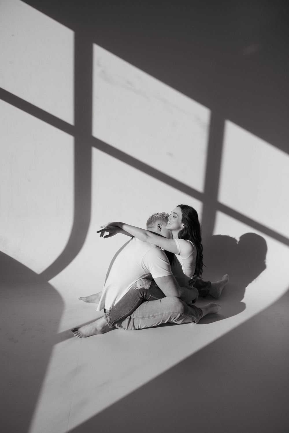An artistic black and white photo of someone sitting in geometric window light patterns.